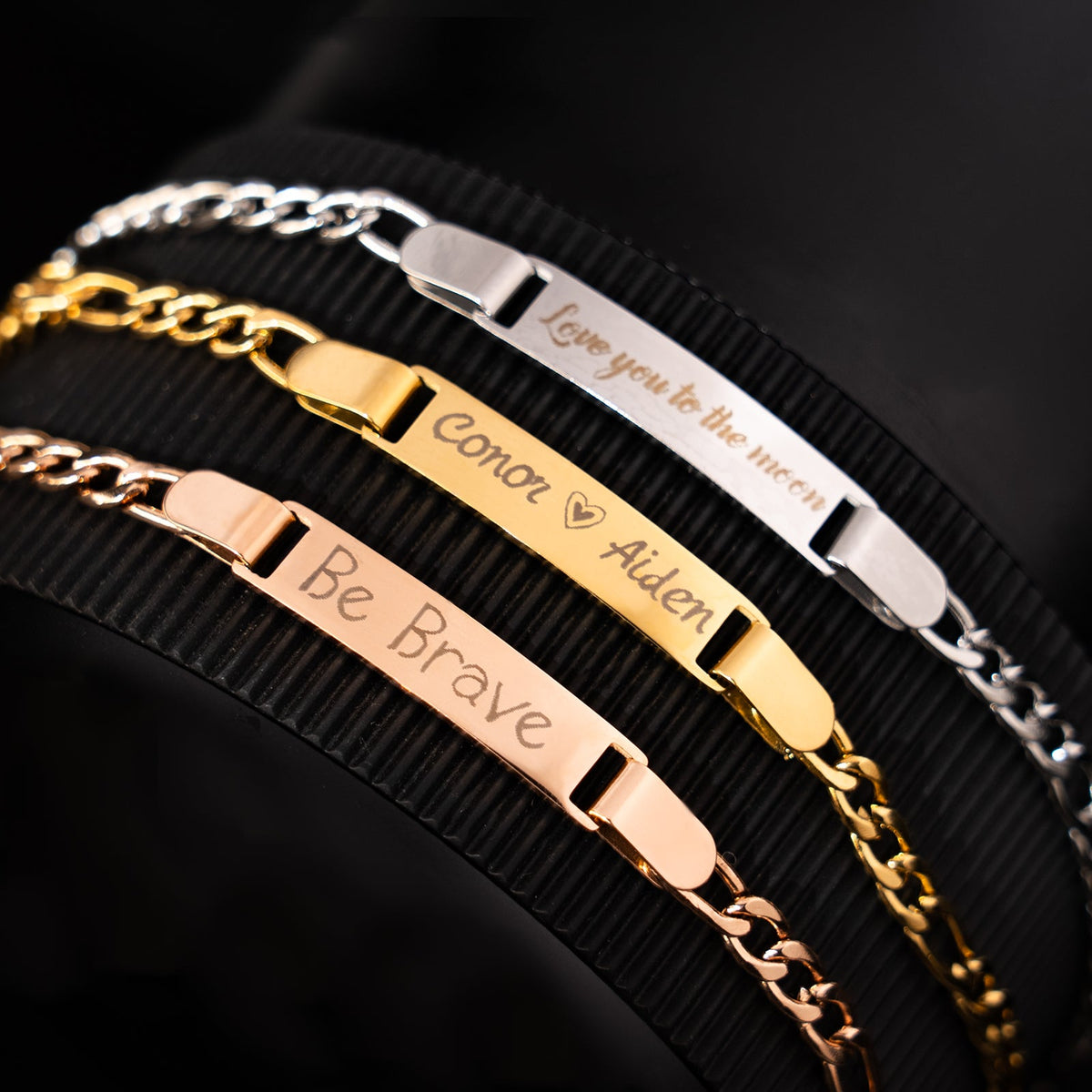 A set of three laser-engraved stainless steel bar bracelets in rose gold, gold, and silver finishes, featuring personalized engravings including "Be Brave", "Conor Aiden", and "Love you to the moon", demonstrating the custom engraving possibilities of these jewelry blanks.