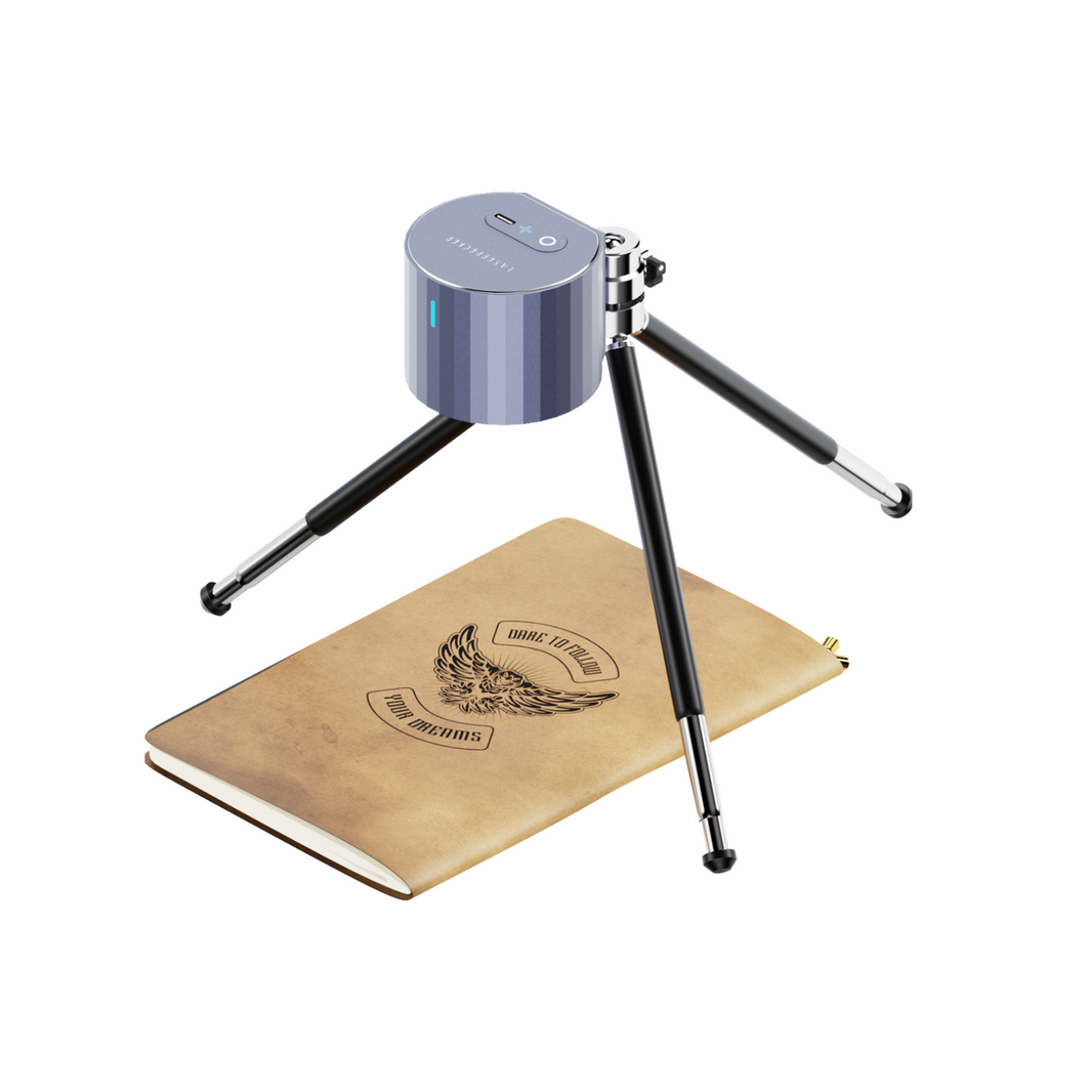 LaserPecker portable cylindrical engraver mounted on a tripod, engraving a custom design onto a notebook cover, bundled with a free 3-piece materials kit for immediate creative use.