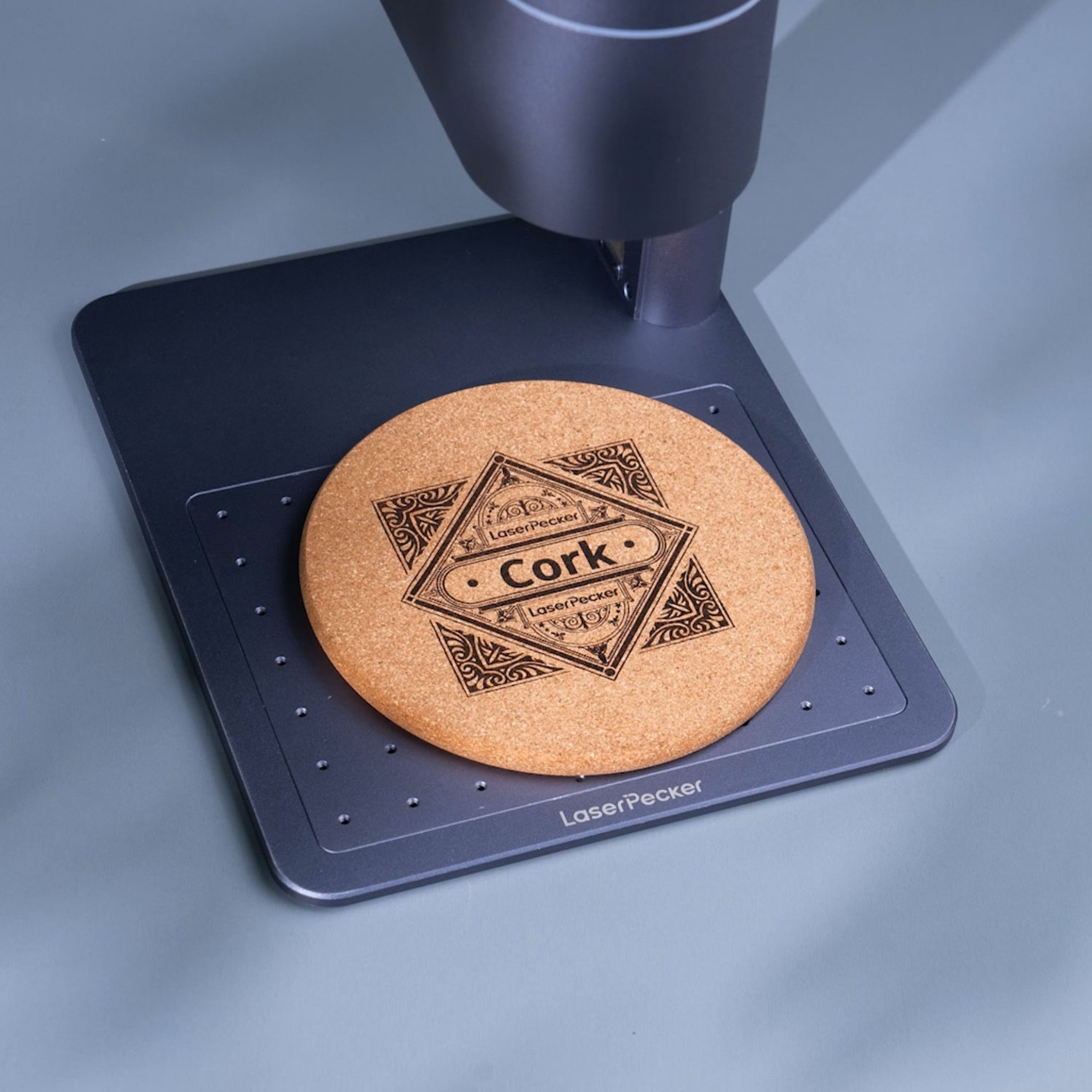 LaserPecker handheld engraver creating a geometric and text design on a cork coaster on the positioning plate.