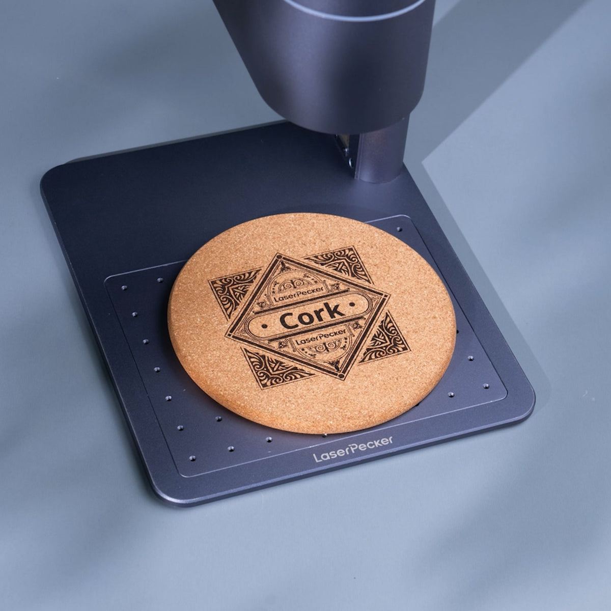 LaserPecker handheld engraver creating a geometric and text design on a cork coaster on the positioning plate.