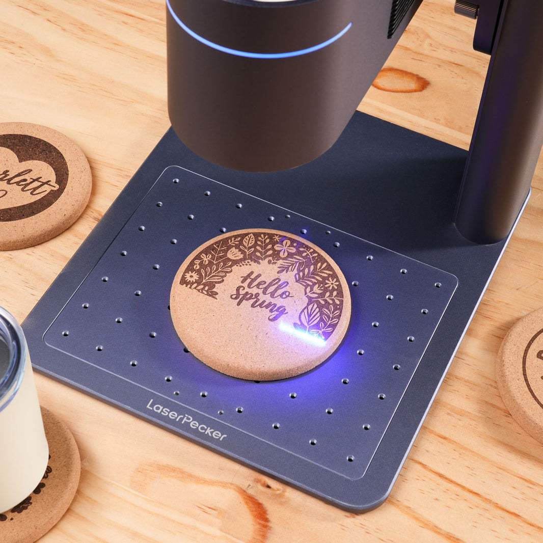 LaserPecker portable laser engraver burning a spring floral design onto a cork coaster on the workbench.